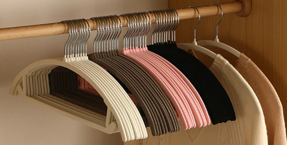 Non-slip velvet hangers in multiple colors for organizing clothes in a wooden wardrobe.