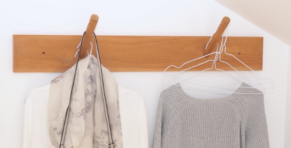 Wall-mounted wooden clothes bar with wire hangers, a gray sweater, and a scarf in a minimalist home setting.